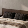 Pair of premium black pillows styled on a bed in a modern minimalist bedroom with a dark wood headboard and raw concrete wall.