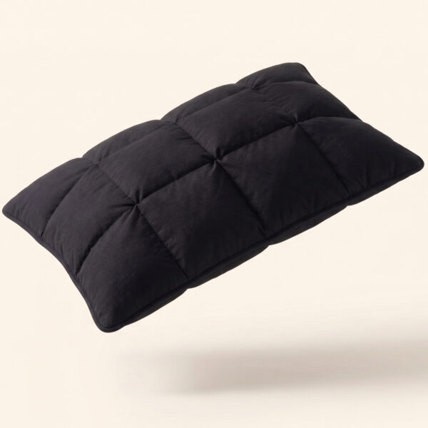 The Black Pillow Original dynamic angled studio shot showing the premium black quilted design on a soft cream background.